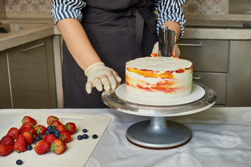 A woman Confectioner decorates a cake with colored cream using a metal spatula. Home confectionery, small business