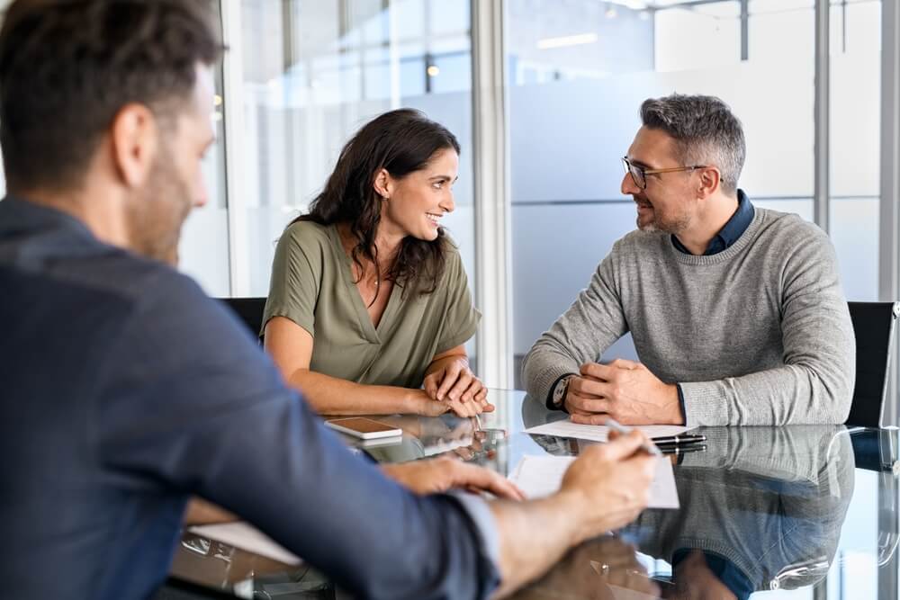 Mature couple discussing in meeting with bank manager for loan. Mature man and woman looking at each other while they are on a visit with a businessman. Happy couple talking amongst themselves