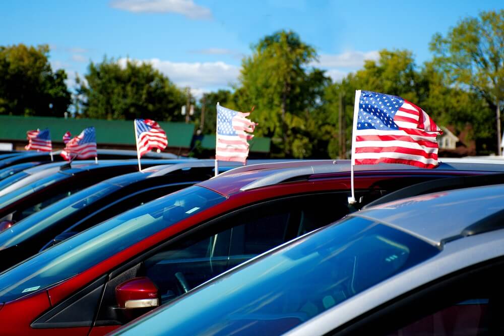 cars at a dealership lined up each has a small American flag on it
