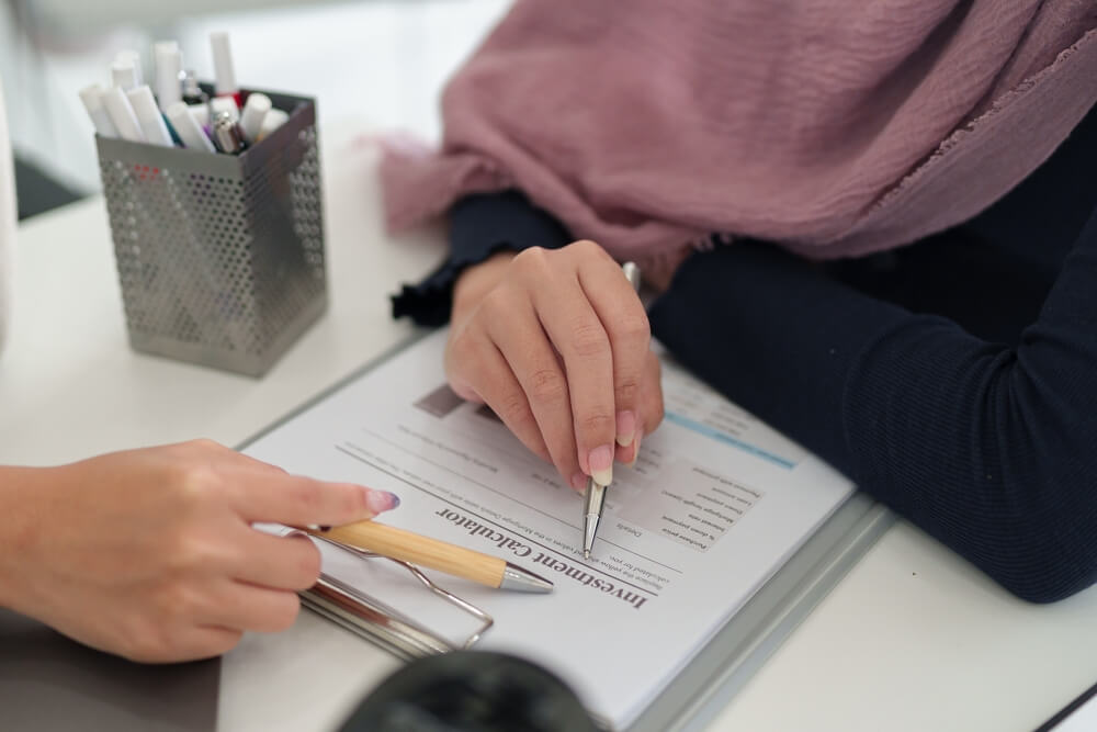 Adult Asian Muslim business woman in hijab reviewing financial investment calculator. Focus on halal mortgage loan and Sharia compliant business growth. Planning future prosperity and wealth.