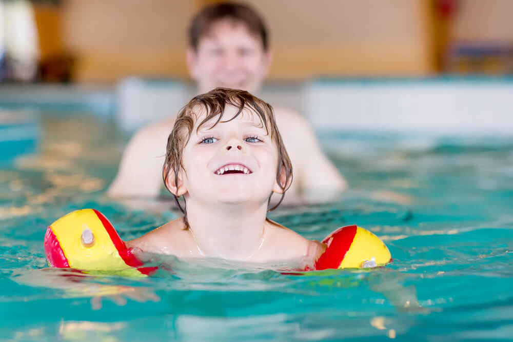 Happy little kid boy and his father swimming in an indoor swimming pool. Active happy kid boy wearing safe swimmies. Family time.