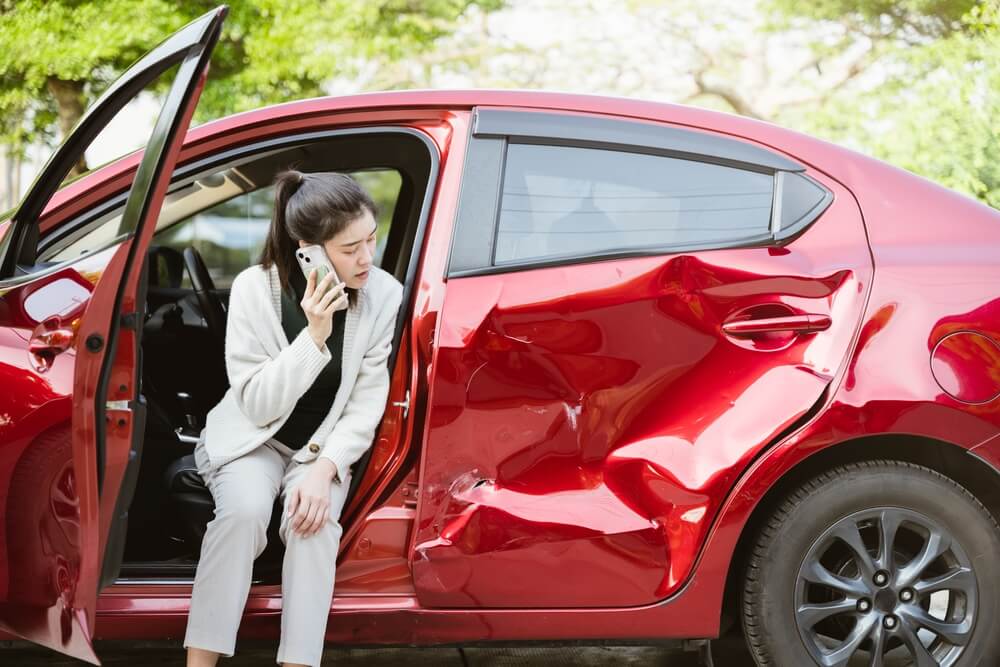 Car accident crash and woman calling insurer on phone