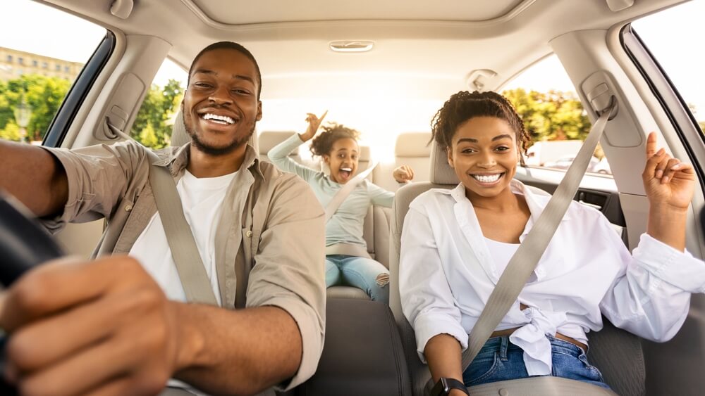 Happy family in a car, looking excited to be going somewhere, lots of trees outside the windows