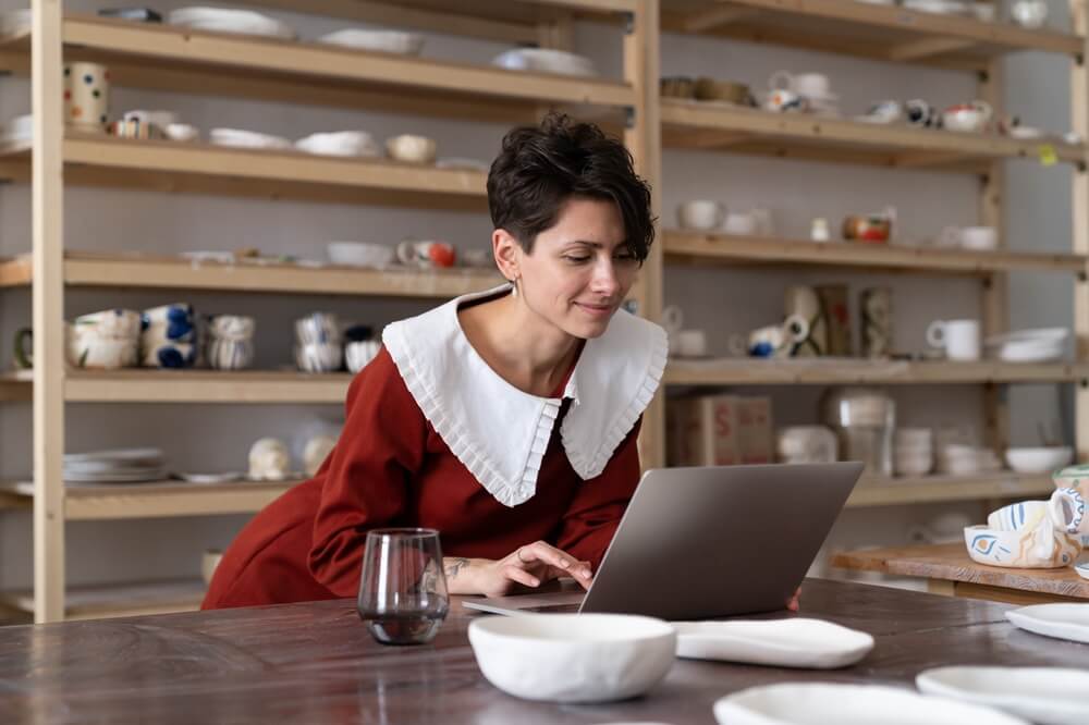 Smiling successful craftswoman ceramic artist on laptop