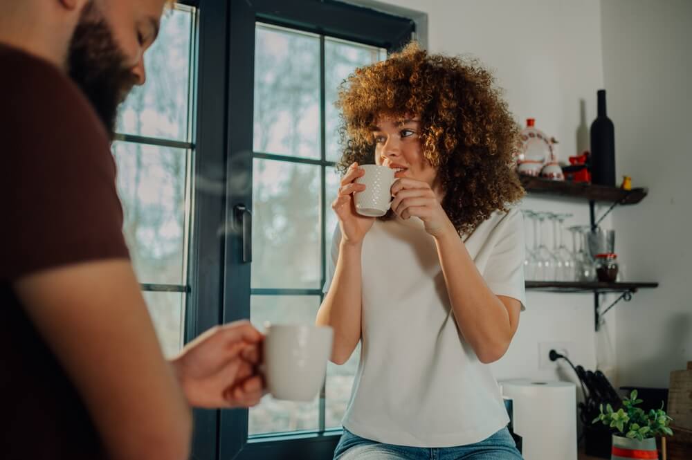 young woman in a neat modern apartment drinking coffee and looking contemplative