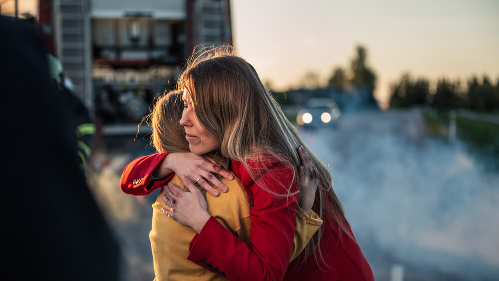 woman/mom hugging child after car accident in background