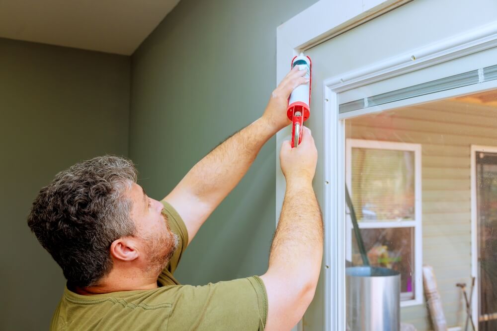 Construction worker installing thermal insulation around window using nail gun