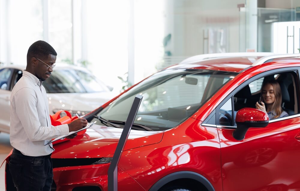 Young woman is happy to buy new red modern car at dealership. Business sale showroom of vehicle.