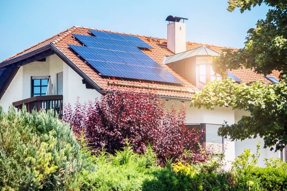 Old House with Solar Panels Station on Roof House with Green Garden. Red Tile Roof With Solar Panel Station on Green Landscape Background