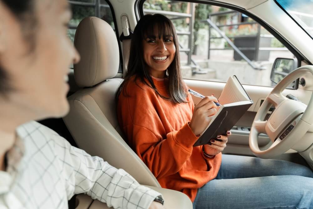Happy young woman taking notes in notebook while sitting in car