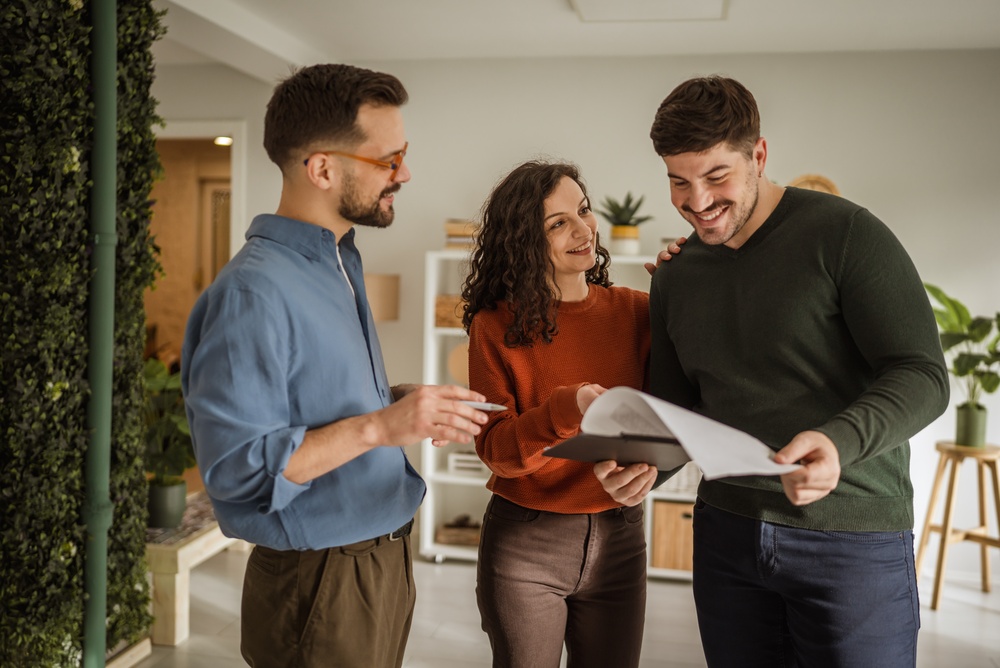 Real estate agent discussing documents agreement terms with happy young couple in modern home