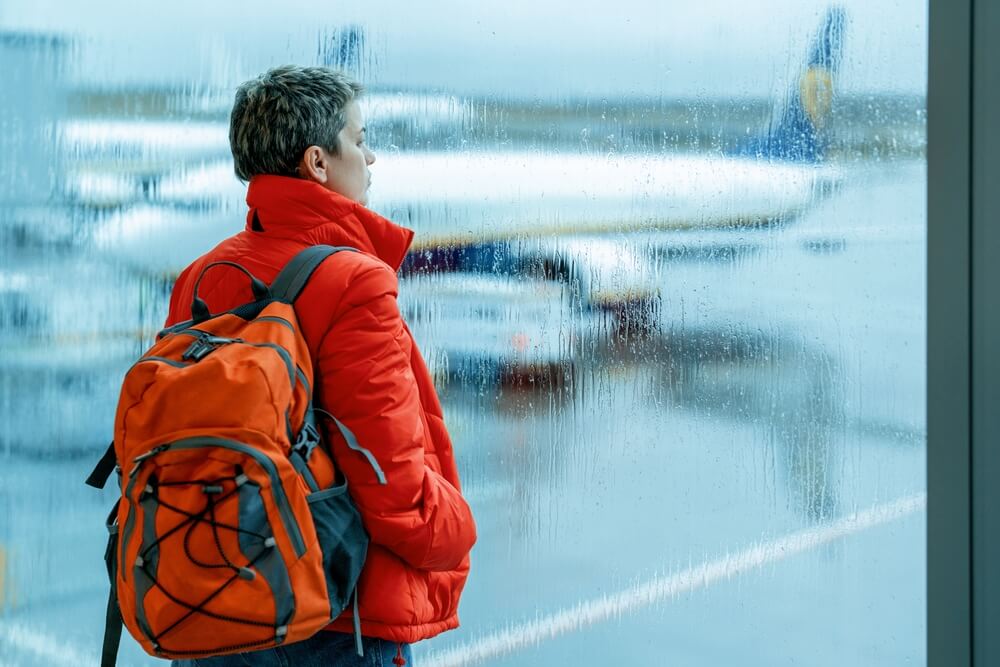 Women with red jacket and backpack waiting at the airport during a rainy day