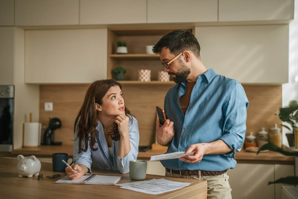 Couple facing financial challenges, calculating expenses, and planning their budget together on the kitchen counter, symbolizing stress and careful money management at home