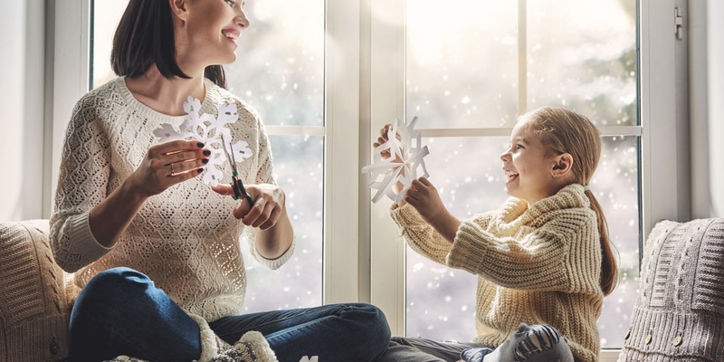 A mother and child cut out paper snowflakes by the window