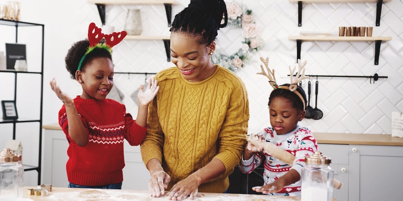 A mother and two small children wearing antlers make cookies