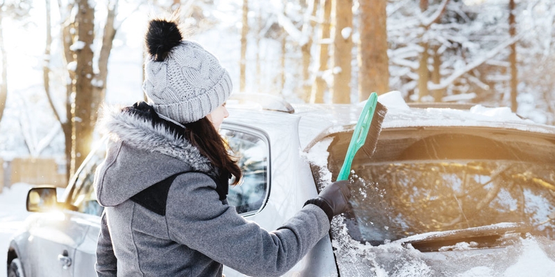 A woman brushes snow off her silver vehicle