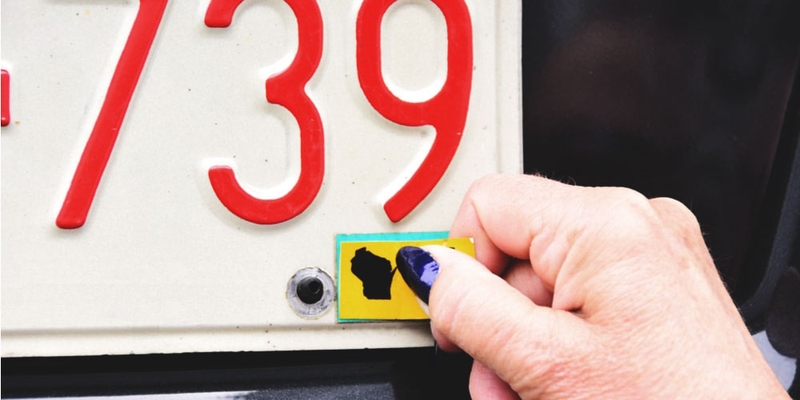 A hand removes an Alberta licence plate sticker