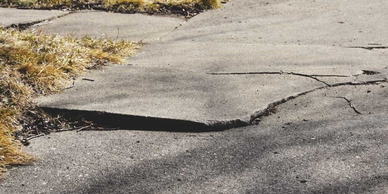 An uneven sidewalk has a crack running through the middle of it