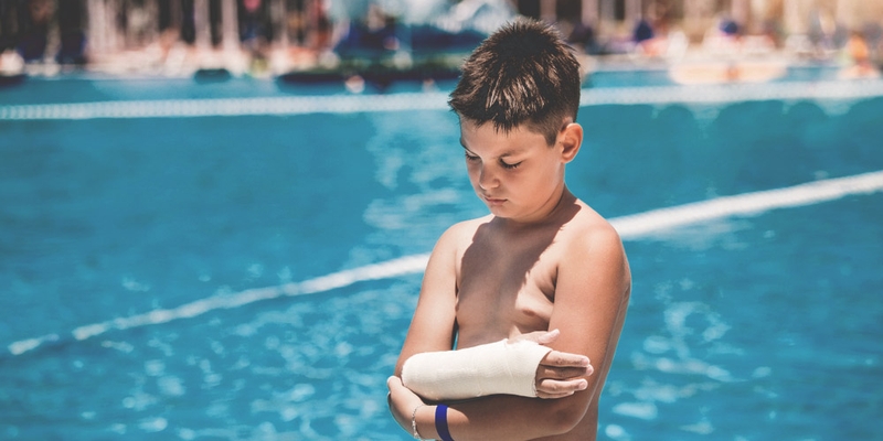 young boy grumpy with a broken arm by a pool