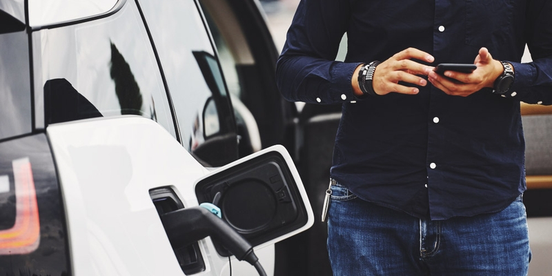 driver waits looking at their phone by white ev while it charges