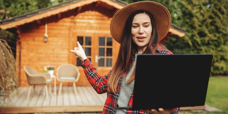 A woman stands with her laptop in hand outside an outbuilding