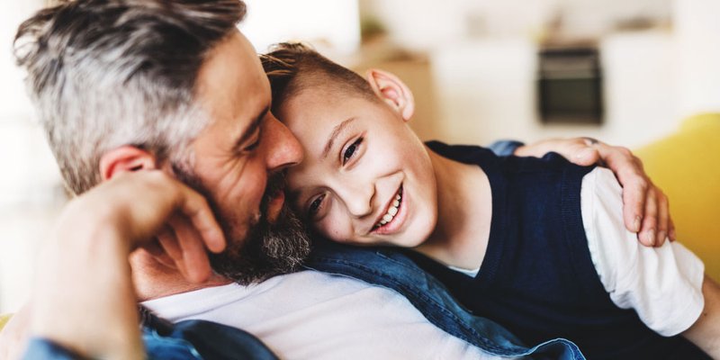 A son snuggles into his dad on the couch at home