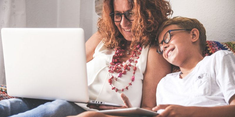 A mom and her son look at something on their laptop while relaxing at home on the couch