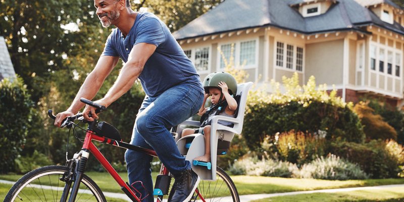 A dad bikes through his neighbourhood with his child in a bike seat behind him