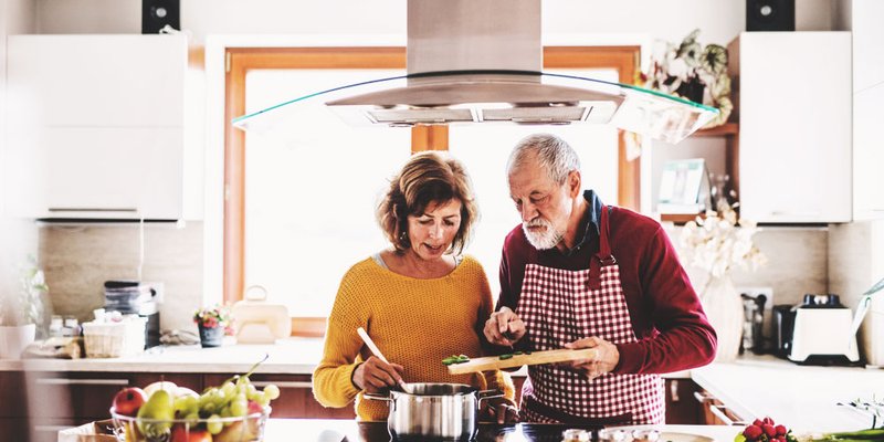 An older couple stirs a pot of sauce while cooking together in their bright modern kitchen