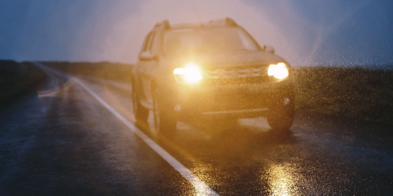 The headlights of a vehicle shine while driving on a road at dusk