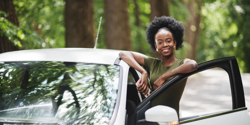 A woman leans on the open door of her vehicle while outside