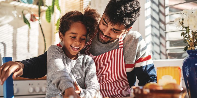 A father and child cracking eggs together in the kitchen