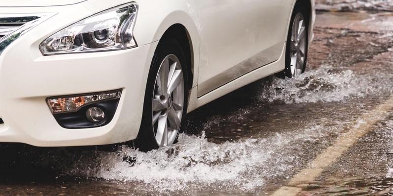 A white sedan drives through a puddle on a rainy wet road