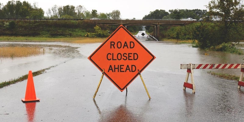 A sign reads Road Closed Ahead on a flooded street