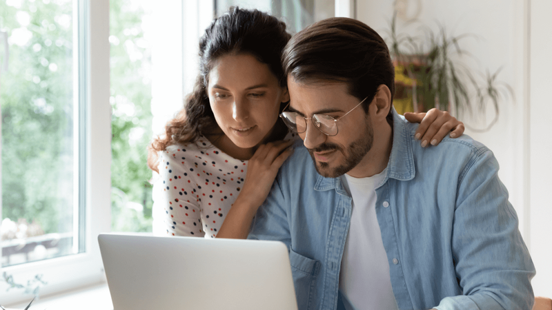 A young couple at home looking at their laptop's screen.