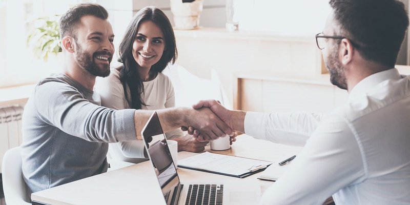 A young couple shakes hands with an advisor or broker at an office
