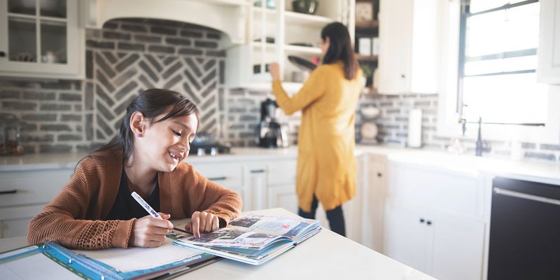 Mother and daughter in modern kitchen while daughter works on her homework at kitchen island