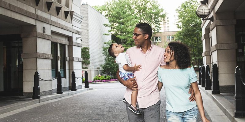 Young modern family with parents and baby son walking downtown in the city
