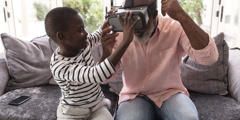Grandson helps grandpa with virtual reality headset in living room