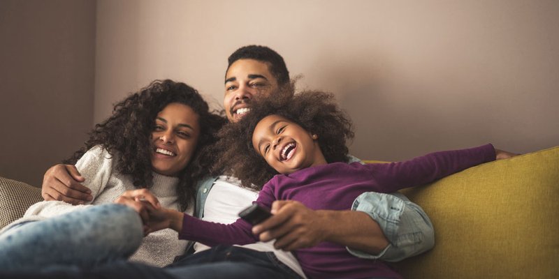 Happy family cuddles on couch together watching tv