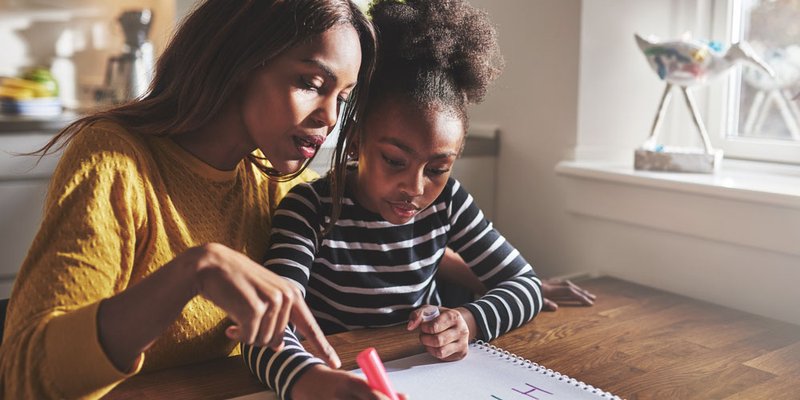 mom helps her daughter with her alphabet at kitchen table