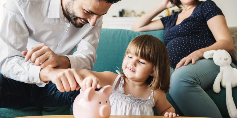 family teachers their daughter about money and help her put coins in her little piggy bank