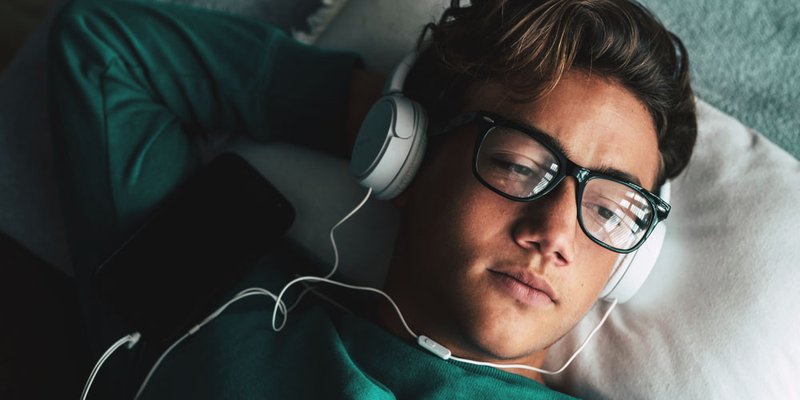 Teenage boy listening to music while laying in his bed