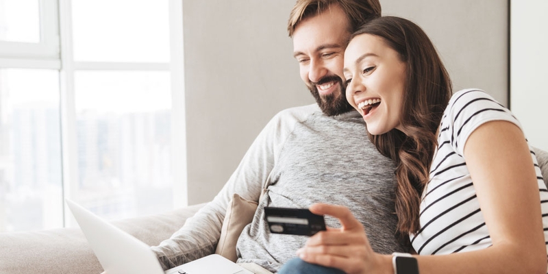 A man and a woman laugh together while online shopping with a credit card
