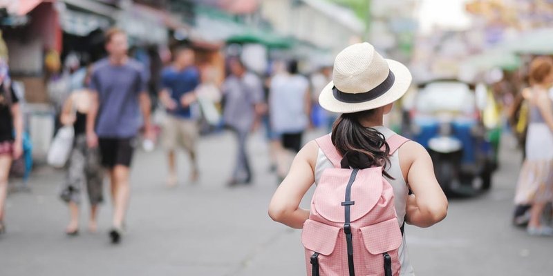 A woman with a pink backpack walks down a busy street
