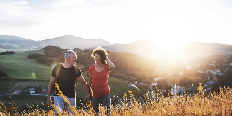 A older woman and man walk up a hill as the sun sets behind them