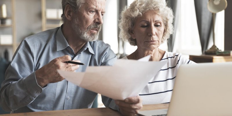 A senior couple review their finances with a laptop and paperwork