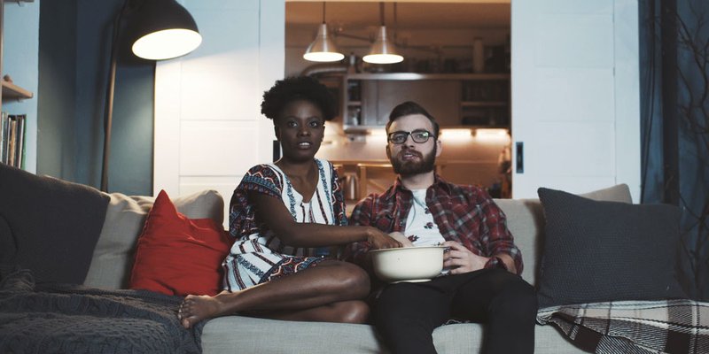 A couple sit on the couch and watch a movie with popcorn