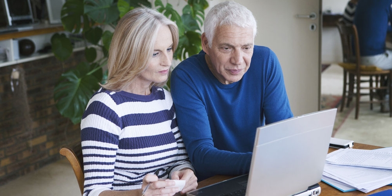 An older couple lean in to look at something on the laptop screen