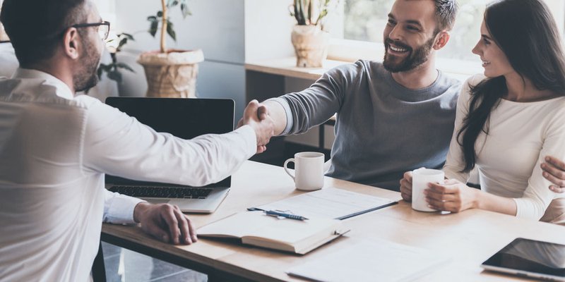 A man embraces his partner and shakes the hand of a financial advisor